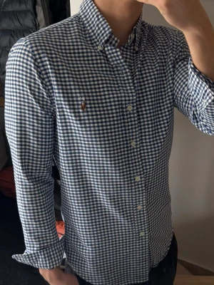 Blårutig skjorta från Polo Ralph Lauren - Säljer en klassisk blårutig skjorta från Polo Ralph Lauren med button-down krage och broderad logga på bröstet. Skjortan har lång ärm, vita knappar och är gjord i mjuk bomull. Perfekt för dig som gillar en tidlös och clean look.