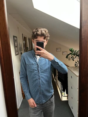 Blå randig skjorta med knappar från Massimo Dutti - Säljer en blå skjorta med vita ränder från Massimo Dutti. Skjortan har klassisk krage, långärmad design och bröstficka. Perfekt för dig som gillar en clean och stilren look. Materialet känns som bomull och passformen är normal.