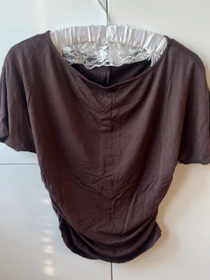Brun topp med spetsdetalj - Snygg brun topp med korta ärmar, Toppens material känns mjukt och lätt, perfekt för en avslappnad stil. Passformen är normal och toppen har en enkel, stilren design. Åtdragen vid midjan.