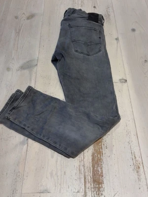 Grå jeans från Replay - Snygga grå jeans från Replay med klassisk femficksmodell och diskret tvättad look. Jeansen har raka ben och normal midja, tillverkade i mjukt bomullsmaterial med stretch för extra komfort. Perfekta för en avslappnad och trendig stil.