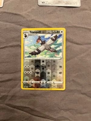 Pokémonkort Tranquill holografisk - Säljer ett Pokémonkort med Tranquill, holografisk design med stjärnmönster. Kortet har gul ram och motivet visar Tranquill flygande i himlen. Text och symboler i svart och silver. Perfekt för samlare eller Pokémonfans.