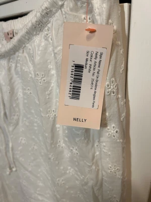 Vita broderade linnebyxor Nelly  - Säljer ett par vita linnebyxor med broderade blommor och hålmönster. Byxorna har breda ben, och dragjustering i midjan för skön passform. Perfekta för en avslappnad och trendig look i sommar.