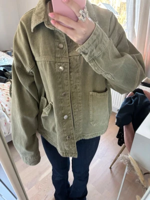 Olivgrön jeansjacka från Zara  - Snygg olivgrön jeansjacka i oversized modell med klassisk krage och silverfärgade knappar. Jackan har två stora framfickor och avslappnad passform som ger en cool och trendig look. Perfekt att slänga över en hoodie eller t-shirt.