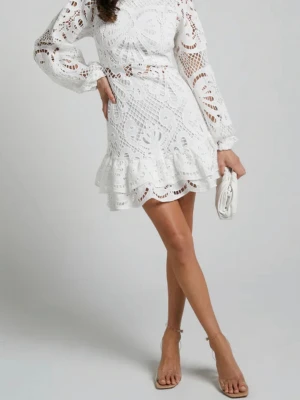 Vit spetsklänning med volang - Helt oanvänd, Kort vit klänning i spets med långärmade puffärmar och volangkant nedtill. Klänningen har hög hals, markerad midja med knytband och ett vackert broderat mönster. Perfekt för dig som vill ha en romantisk och trendig look.