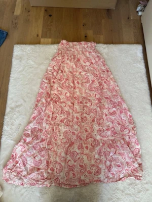 Rosa paisleymönstrad långklänning H&M - Långklänning från H&M i vitt och rosa med paisleymönster. Klänningen har resår i midjan och är tillverkad i ett lätt och luftigt material, perfekt för varma dagar. 