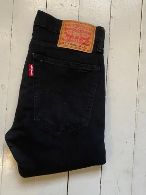 Svarta Levi's 519 jeans - Säljer ett par svarta Levi's 519 jeans med klassisk röd Levi's-tag på bakfickan och läderpatch i midjan. Jeansen har smal passform och raka ben, tillverkade i mjukt denimtyg som sitter snyggt. Perfekta för en trendig och avslappnad stil. Dessa jeans är slim fit. Storleken är w30. Midjebredden är 37cm. Längden är 98cm. Smalben bredden är 16cm. 