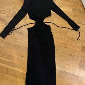 Svart långärmad cut out-klänning - Säljer en svart långärmad klänning med cut out-detaljer i midjan och knytband på sidorna. Klänningen har en kroppsnära passform med axelvaddar. Endast använd vid fåtal tillfällen✨