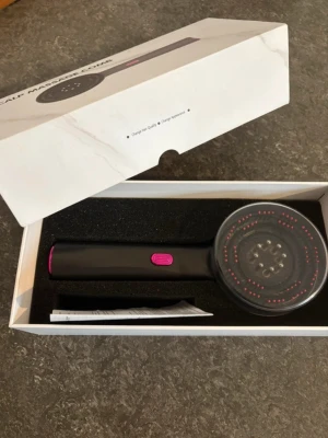 Scalp massage comb svart/rosa - Elektrisk scalp massage comb i svart med rosa detaljer. Rund borste med små massagepiggar och ergonomiskt handtag. Perfekt för att massera hårbotten och stimulera blodcirkulationen. Levereras i originalförpackning med instruktion.