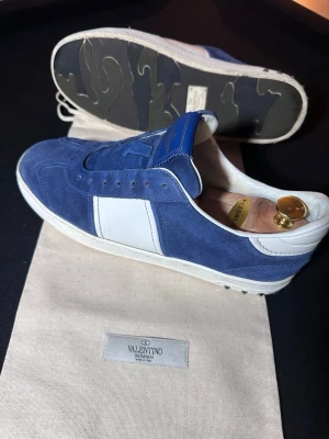 Navy blue Valentino Flycrews - Säljer nu ett par extremt eftertraktade Valentino Flycrews i den marinblå mockan. Denna modell säljs inte längre i butik. Skick & Detaljer: • Utsida: I fantastiskt fint visuellt skick. Mockan är mjuk och fin, och sulorna är rena. • Insida: Det finns ett litet slitage i hälfodret, vilket inte syns medan användning.  • Tillbehör: Säljes som "Fullset" med box, dustbag, skosnören, extra spikar och Authenticity Card. Hör av dig om du vill ha fler bilder på det små defekter som finns.Passar Storlek 43