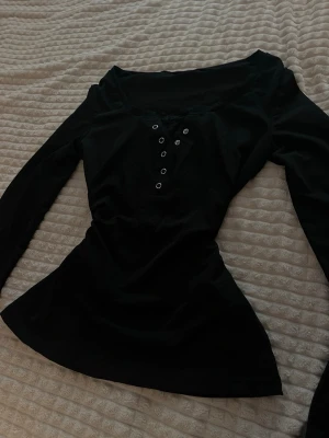 Svart långärmad topp med spets - Snygg svart långärmad topp med knappdetaljer framtill och dekorativ spets vid urringningen. Figurnära passform och mjukt material som känns bekvämt mot huden. Perfekt för dig som gillar en enkel men ändå trendig stil.