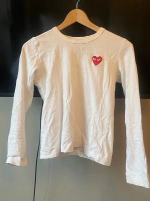 Vit tröja Comme des Garçons - Säljer en vit långärmad topp från Comme des Garçons Play med det ikoniska röda hjärtat med ögon broderat på bröstet. Tröjan har rund halsringning och är gjord i mjuk bomull. Perfekt till jeans eller kjol för en clean och trendig look. Köpt secondhand men har aldrig använt själv pga att den är lite för liten. Storleken är xs men sitter så här på mig som vanligtvis har m. Har två små fläckar på framsidan som inte syns så mycket❣️