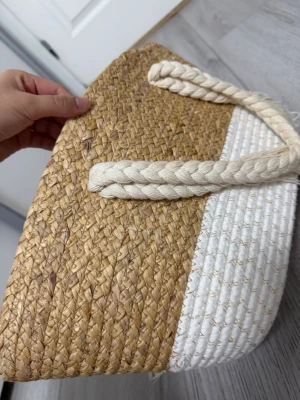 Strandväska i halm och vitt rep - Snygg shoppingväska i flätad halm och vitt rep med guldtråd. Väskan har rejäla, flätade handtag i vitt och en oval botten i vitt rep. Perfekt för dig som gillar naturliga material och en somrig look.