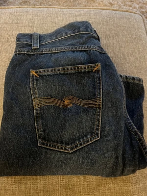  Nudie Gritty Jackson - Snygga mörkblå jeans från Nudie Jeans Co i klassisk femficksmodell med orangea sömmar och ikonisk broderad bakficka. 