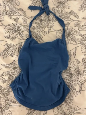 Blå halterneck topp - Snygg blå halterneck topp med knytning i nacken. Toppen har en enkel, figurnära passform och är tillverkad i ett mjukt, stretchigt material. Perfekt för att skapa en trendig och avslappnad look.