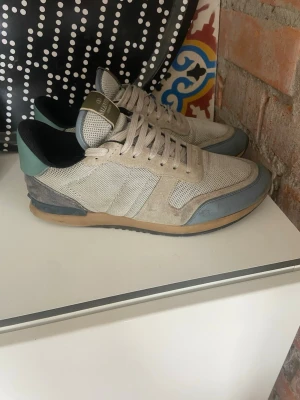Valentino rockrunners - Snygga sneakers från Valentino i beige mesh och mocka med blå och grå detaljer samt mintgrön häl. Gummisula i beige och blått med nitar baktill. Skön passform och cool design som sticker ut. Storlek 42, använda en del men inga stora skador, se defekt på bild 4.
