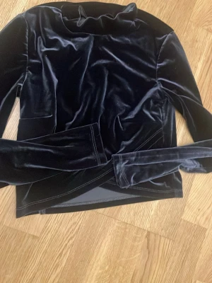 Mörkblå sammets polotopp - Mjuk och lyxig mörkblå polotopp i sammet. Toppen har långa ärmar och en hög krage som ger en elegant look. Perfekt för dig som vill ha något extra till din outfit. Materialet är glansigt och känns riktigt skönt mot huden.