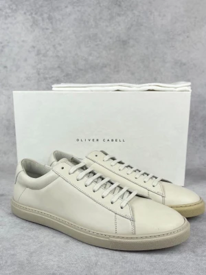 Vita sneakers från Oliver Cabell - Stilrena vita sneakers från Oliver Cabell i mjukt läder. Klassisk låg modell med vita snören och diskret design. Yttersulan och skon har en minimalistisk look som passar till det mesta. Perfekta för dig som gillar clean och enkel stil. Grå bege färg säljs pga passar inte mig