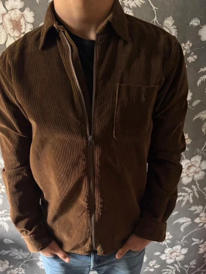 Ralph lauren jacka brun  - Snygg brun overshirt ralph lauren i manchestertyg med dragkedja framtill och en bröstficka. Klassisk krage och raka ärmar ger en clean look. Perfekt att slänga över en t-shirt för en avslappnad stil. Köpt i butik inga slitage alls 