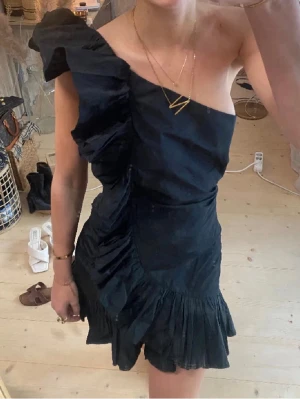 Svart oneshoulder volangklänning - Supersnygg svart kortklänning med oneshoulder och stora volangdetaljer längs axeln och ner över klänningen. 