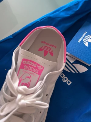 Adidas x Balenciaga vita sneakers 38  - Snygga vita sneakers från Adidas och Balenciaga med rosa detaljer på plösen och insidan. Klassisk låg modell med vita skosnören och diskret branding. Tillverkade i slätt läder för en clean och modern look.