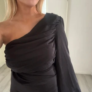 Superfin balklänning - Säljer denna superfina svarta balklänning med en arm. Den är aldrig använd utan endast testad på och har prislappen kvar. Säljer den då jag inte kommer få användning av den. Jag är 165 cm🤗💞