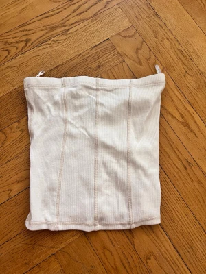 Vit ribbad tubtopp från H&M Divided - Säljer en vit ribbad tubtopp från H&M Divided i storlek XS. Toppen har en enkel och clean design med vertikala sömmar framtill och är perfekt för sommardagar. Materialet är mjukt och stretchigt för en bekväm passform.