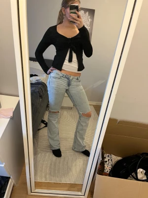 Svart croppad bolerotopp med knyt - Svart bolerotopp med lång ärm och v-ringning. Toppen är croppad och har en snygg knytning framtill. Perfekt för lager-på-lager och ger en trendig siluett. Materialet känns mjukt och följsamt.