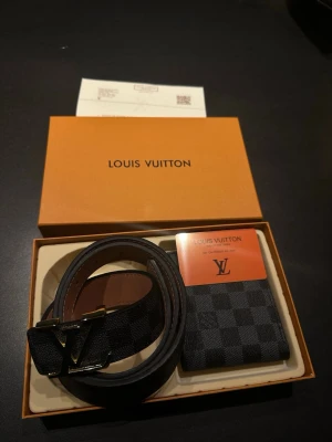 Svart bälte med spänne - Säljer ett svart mjuk plånbok och bälte med klassiskt rutigt mönster och ett spänne i guld. Bältet är gjort i skinn och har en exklusiv känsla som passar till många olika outfits. Kommer i originalask.