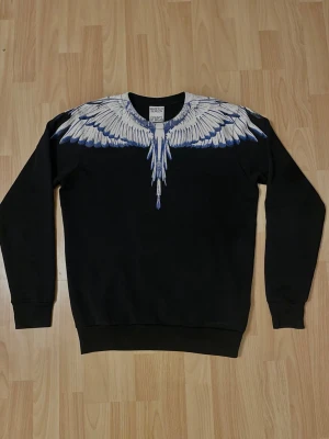 Marcelo Burlon tröja - Marcelo Burlon sweatshirt färg svart med vitt och blå design i storlek XS, men passar som S. Den är i väldigt bra skick och äkta. Kommer med original dustbag, samt så finns mått vid förfrågan. Prisförslag och frågor är välkomna 🙏💬