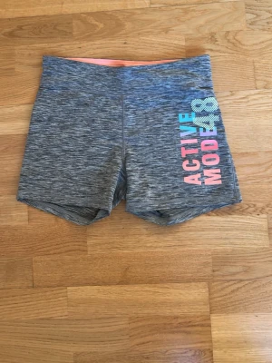 Grå träningsshorts ACTIVE MODE - Gråmelerade träningsshorts med trycket 'ACTIVE MODE' i blått och rosa på ena benet. Shorts med tight passform och bred resår i midjan. Perfekta för gymmet eller löprundan.
