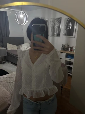 Vit volangblus med prickigt mönster - Söt vit blus med volangkant nedtill och diskret prickigt mönster. Blusen har v-ringning, spetsdetaljer och långa ärmar i transparent material. Perfekt att styla med jeans för en trendig look. Passar mig som har storlek xs och förmodligen kommer de passa för personer med xs-s 