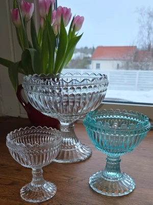 Tre glasskålar på fot - Säljer tre dekorativa glasskålar på fot i olika storlekar. Två är klara och en är turkos. Snygga att ha framme som dekoration i köket eller vardagsrummet. Den lilla är från Marimekko & dom två större än märke okänt. 