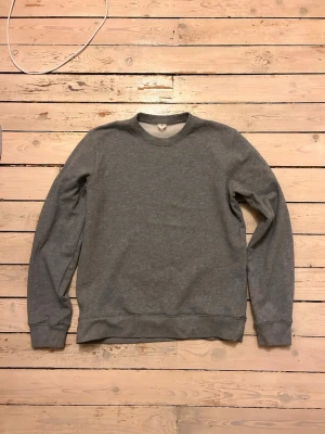 Grå basic sweatshirt Arket - En enkel och stilren grå sweatshirt med rund halsringning och långa ärmar. Tröjan har ribbade muddar vid ärmslut och nederkant. Perfekt för en avslappnad look och passar till det mesta i garderoben.