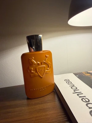 Parfums de Marly parfym Althaïr flaska - Exklusiv parfym från Parfums de Marly i en snygg orange flaska med silverfärgat lock. Flaskans framsida har ett upphöjt emblem med två hästar och texten '1743'. Perfekt för dig som gillar lyxiga dofter och stilren design.