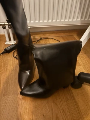 Svarta höga stövlar med spetsig tå - Säljer ett par svarta stövlar med högt skaft och spetsig tå. Stövlarna har en slät finish och är tillverkade i ett material som liknar läder. Perfekt för dig som vill ha en edgy och trendig look.