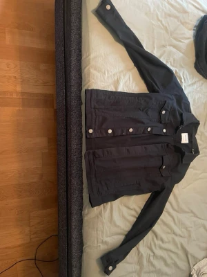 Svart jeansjacka från Jack & Jones - Snygg svart jeansjacka från Jack & Jones med klassisk krage och silverfärgade knappar framtill. Jackan har två bröstfickor med lock och knapp samt raka ärmslut med knapp. 