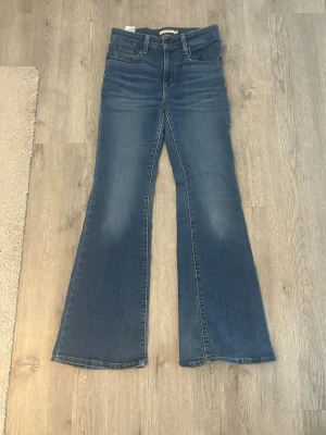 Blå bootcut jeans från Levi's - Säljer ett par klassiska blå bootcut jeans från Levi's med fem fickor och normalhög midja. Jeansen har en snygg tvätt med lätt slitning och utsvängda ben. Perfekta för dig som gillar retrostil och vill ha ett par bekväma jeans i mjukt denimtyg.