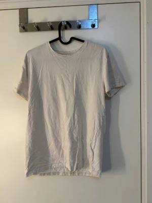 Vit basic t-shirt i bomull - Enkel vit t-shirt med rund hals och korta ärmar. Modellen är rak och klassisk, perfekt för en avslappnad stil. Tillverkad i mjuk bomull som känns skön mot huden.