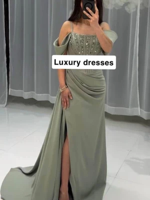 Klänning fest/ bal - Elegant ljusgrön långklänning med offshoulder och smala axelband. Klänningen har vackra pärldetaljer på livet, markerad midja och en slits framtill. Perfekt för bal eller festliga tillfällen. Materialet har ett mjukt, flytande fall.