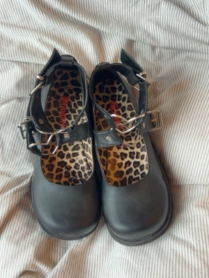 Demonia Sprite-02 svart - Använts 2/3 gånger under en väldigt kort tid! Unika svarta loafers med chunky platåsula och dubbla remmar med silverfärgade spännen. Insidan har ett coolt leopardmönster som ger extra edge. Perfekta för dig som vill sticka ut och gillar alternativ stil. Det är US storlek 10 men skulle säga att de passar storlek 40-42!❤️