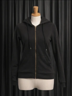 Svart zip hoodie med fickor - Klassisk svart hoodie med dragkedja framtill och två stora fickor. Tröjan har huva med dragsko och ribbade muddar vid ärmslut och nederkant. Tillverkad i mjukt och tunt material, perfekt för lager på lager. Passar till det mesta och är superenkel att styla.