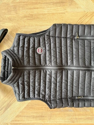 Svart dunväst från Colmar - Snygg svart dunväst från Colmar med quiltad design och två dragkedjeförsedda fickor framtill. Västen har en hög krage och ett Colmar-märke på bröstet. Insidan är ljusgrå vilket ger en schysst kontrast. Perfekt för lager-på-lager och streetwear.