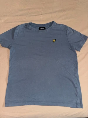 Blå t-shirt från Lyle & Scott - Snygg blå t-shirt från Lyle & Scott med klassisk gul logga på bröstet. T-shirten har rund halsringning och korta ärmar. Tillverkad i mjuk bomull som känns skön mot huden. Perfekt för en avslappnad och stilren look.