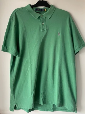 Grön pikétröja från Polo Ralph Lauren - Snygg grön pikétröja från Polo Ralph Lauren med klassisk krage och knappar framtill. Tröjan har korta ärmar och den ikoniska broderade loggan på bröstet. Perfekt för en avslappnad och stilren look.