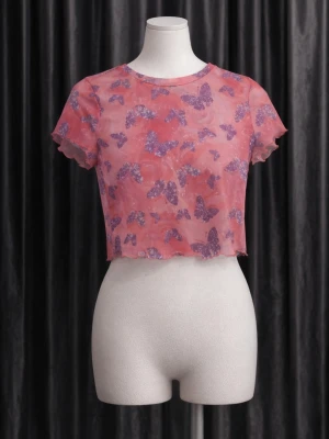 Rosa croppad mesh topp med fjärilar - Trendig croppad topp i meshmaterial med rosa bas och lila fjärilsmönster. Toppen har korta ärmar och vågiga kanter för en cool look. Perfekt för dig som vill sticka ut med färg och mönster.