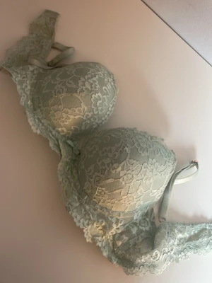 Ljusgrön spets-bh med rosett - Söt ljusgrön push up bh med vacker spets över hela plagget. Dekorerad med en liten rosett mellan kuporna och breda spetsband. Perfekt för dig som gillar pastellfärger.