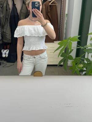 Vit offshoulder topp med spetsvolang - Säljer en söt vit offshoulder topp med bred spetsvolang och smockad midja. Toppen har inga axelband och är därför offshoulder. Perfekt för dig som gillar somrig stil.