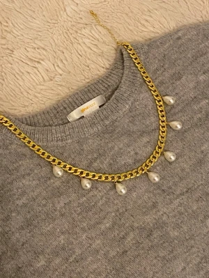 Guldfärgat halsband med pärldroppar - Snyggt halsband i guldfärgad rostfritt med sex droppformade pärlor som hänger längs kedjan. Kedjan har en chunky design och justerbar längd. Perfekt för att ge din outfit en trendig touch.