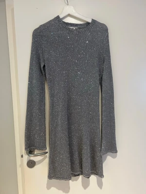 Monki -glittrig silverklänning  - En snygg stickad klänning i silver med glittereffekt och lång ärm. Klänningen har en rak passform och rund halsringning. Materialet är stickat med inslag av glittrande tråd som ger en cool shimmer. Perfekt för dig som vill sticka ut med en metallic look.
