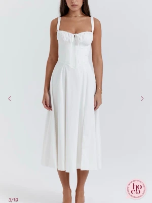 Vit midiklänning med slits - Säljer en vit midiklänning med breda axelband, rynkad byst och knytning framtill. Klänningen har en markerad midja och en hög slits på ena sidan för en trendig look. Tillverkad i ett lätt, mjukt tyg som faller snyggt. Ordinarie pris 2000kr 